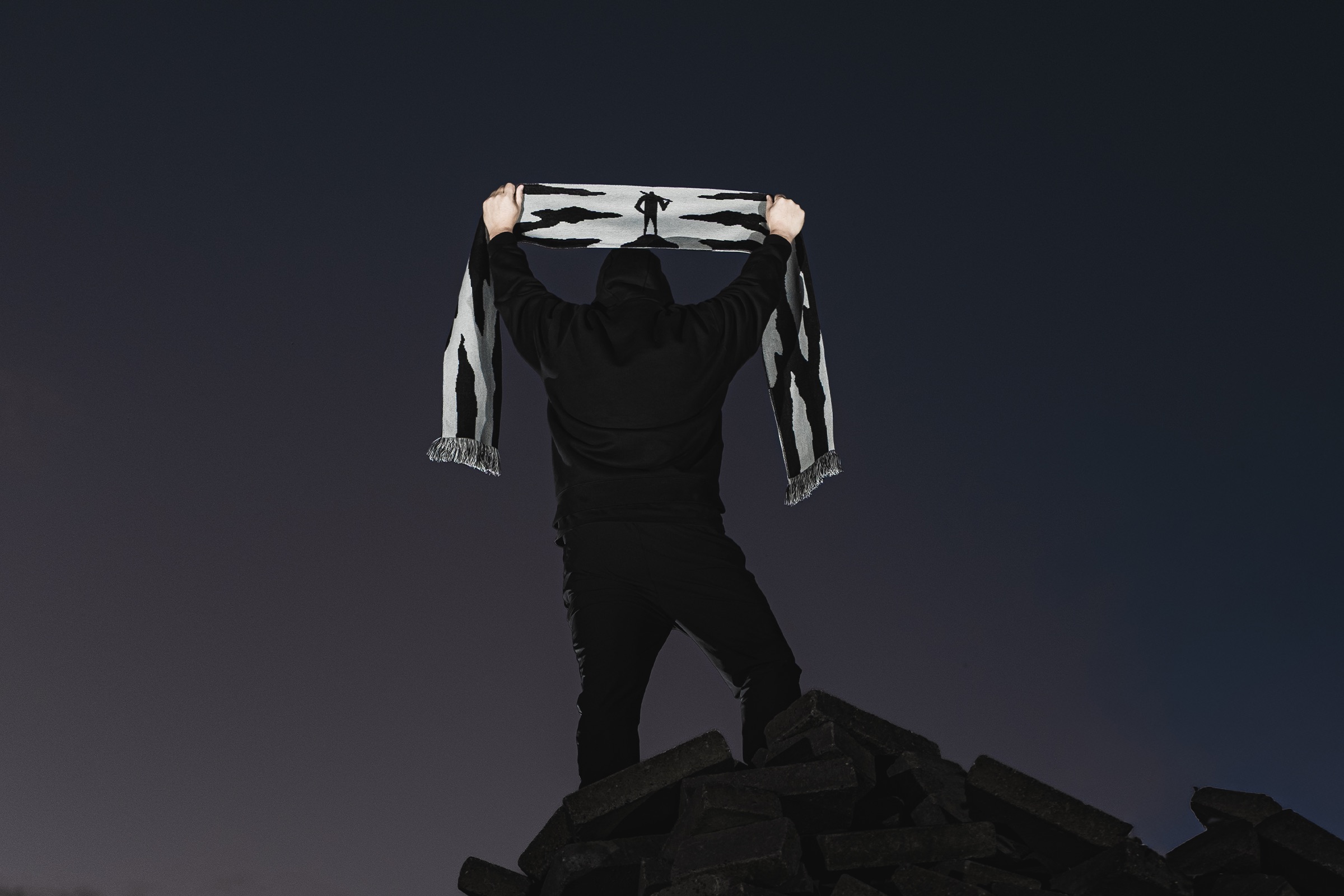 Fan holding up a League Extraordinaire scarf, standing on a pile of rubble
